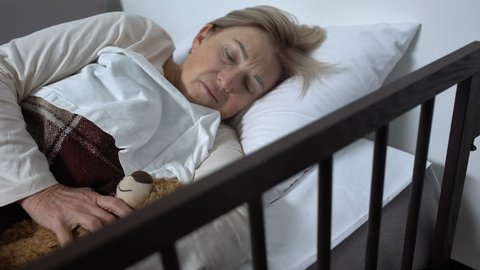 Weak woman lying on sickbed in hospital hugging toy-bear, hope for recovery