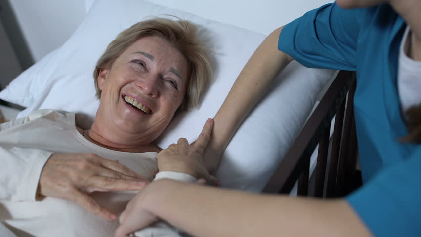 Caring nurse telling jokes to old female patient lying in sickbed rehabilitation Royalty-Free Stock Footage #1028391071