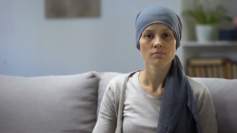 Woman after chemotherapy sitting at home and looking into camera, background