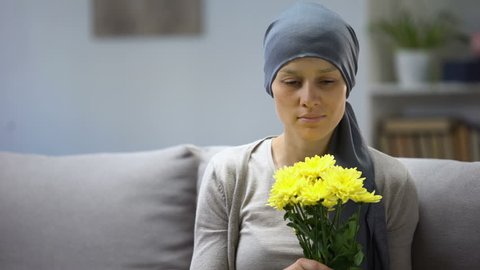 Recovery after cancer, woman in headscarf smelling flowers and enjoying life