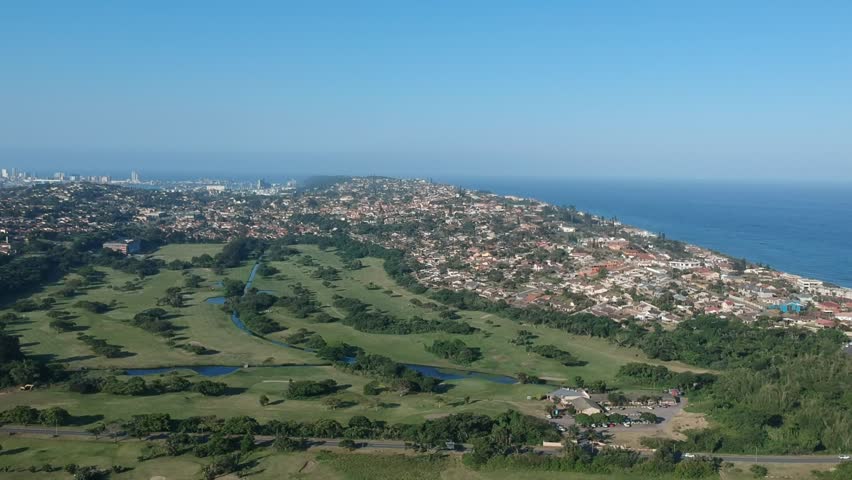 Ascending aerial view of a residential area on a hillside near the coast. Beautiful azure sea and bright sky on the horizon. Scenic beauty of Durban, South Africa.