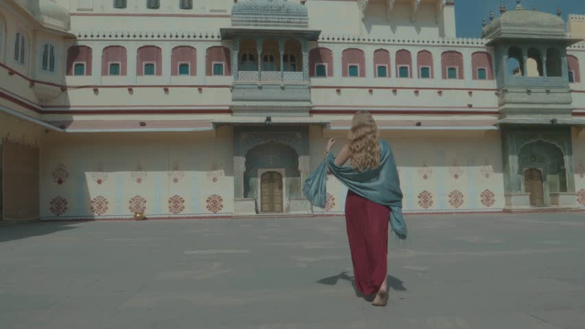Beautiful blonde woman in a red dress walking through the court yard of the City Palace in Jaipur with stunning traditional architecture