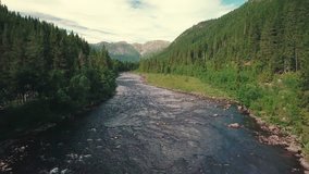 Forward panning drone shot over a river and gradually crane down, next to a road in a forest . Mountains are shown in the bachground. 4k quality video in Norway