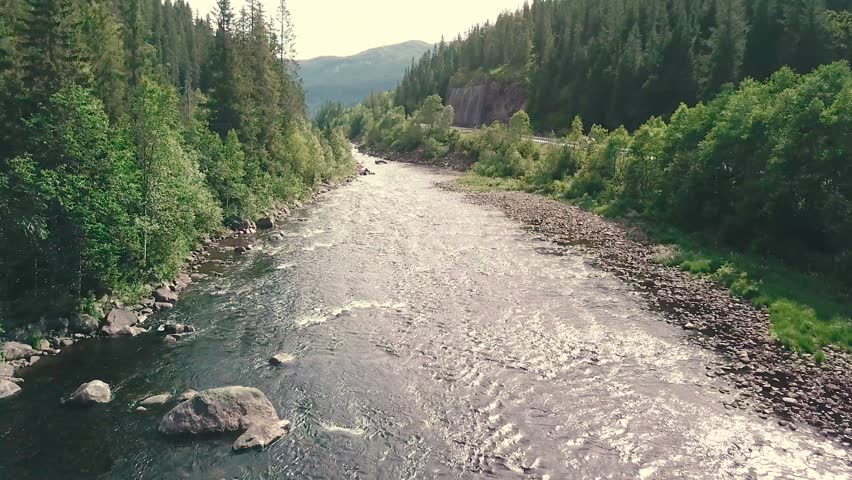Close forward drone shot over a river next to a road in a forest. Mountains are shown in the bachground. 4k quality video in Norway