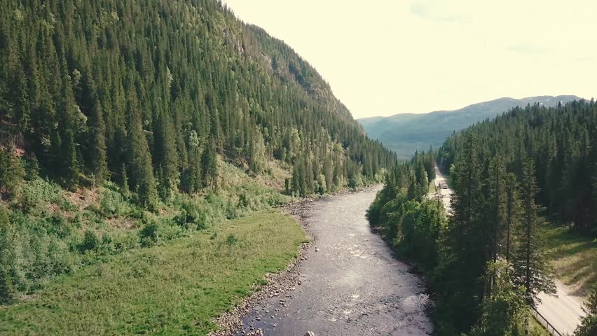 Elevating tilt down forward drone shot over a river next to a road in a forest. Mountains are shown in the bachground. 4k quality video in Norway