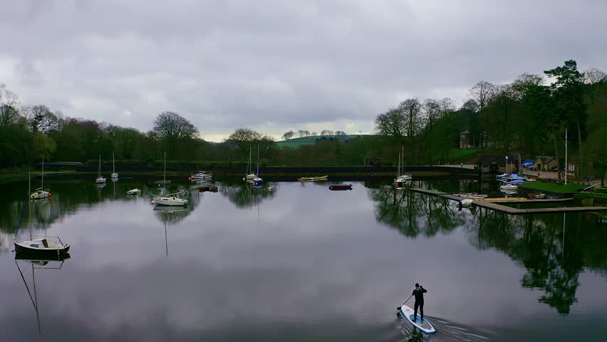 Beautiful aerial view, footage of middle aged man paddle boarding on Rudyard Lake in the Derbyshire Peak District National Park, popular holiday, tourist location with peaceful calm water