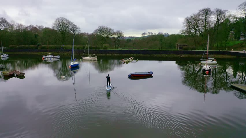 Beautiful aerial view, footage of middle aged man paddle boarding on Rudyard Lake in the Derbyshire Peak District National Park, popular holiday, tourist location with peaceful calm water