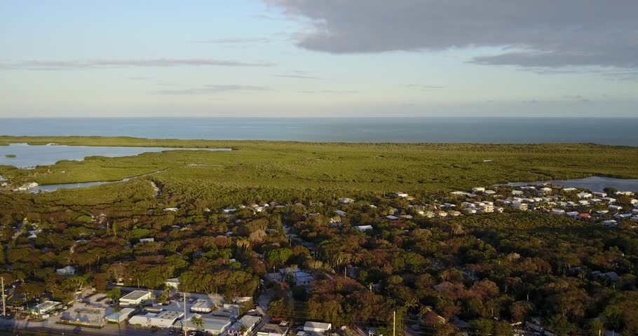 AERIAL: slow and wide push over the suburban area towards the unique mangrove terrain found in Key Largo, Florida during golden hour.
