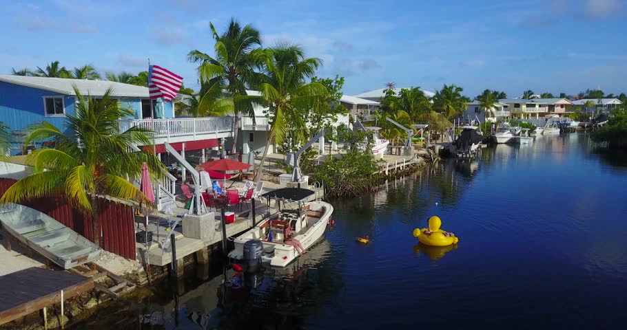 AERIAL: lifting away from a set of adults playing with inflatable toys in the canal to reveal more of Key Largo, Florida.