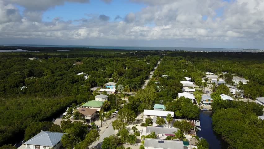 AERIAL: pushing in the direction of a street surrounded by greenery and suburban terrain found in Key Largo.