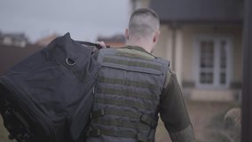 The young man in military closes with big bag entering the gate and walking toward the big house. A man returns from the military service home. Leaving from war. Back view - Powered by Shutterstock - Get 15% off with code: PIKWIZARD15