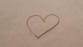 4k video. Top view on hand drawing heart on wet sand. Template for Valentines day, wedding, love. Heart is washed away by a sea wave on a sandy beach. 