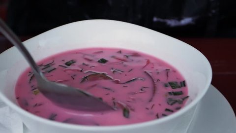 a bowl with red beetroot soup, lifting spoon in slow motion