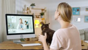 Medium shot of woman holding cute cat and video calling her vet on computer. She is talking and asking for advice