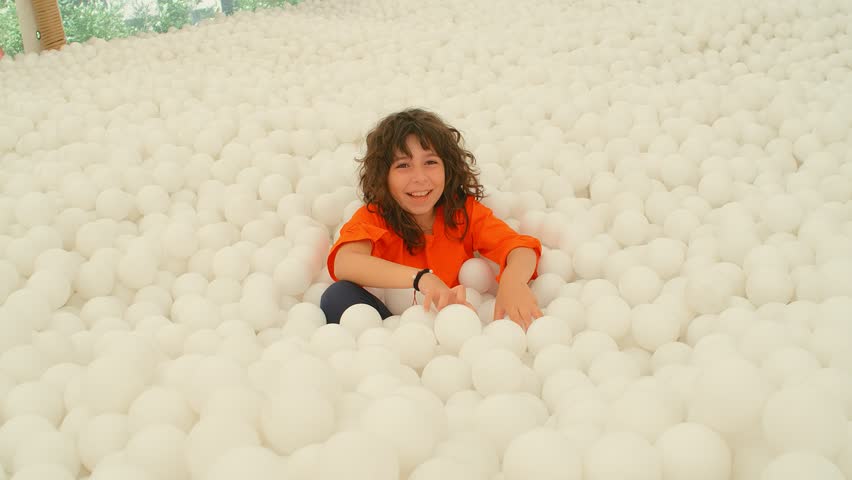 A cute 9-10 years old girl having fun among lots of white ball in a ball pit. 4k slow motion