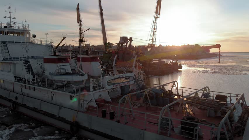 the parking of ships, boats, construction barges in the port on the river, ice melting, sunset time, aerial filming from the rotor