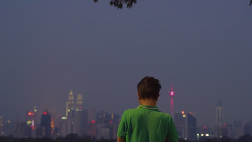 A young Asian man enjoying Kuala Lumpur cityscape view, night scenery.