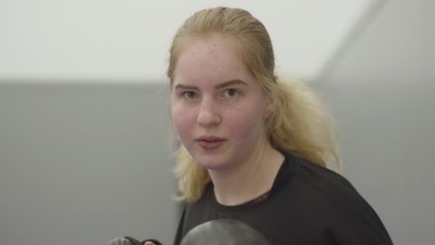 Portrait young blond girl panching on camera in boxing gloves