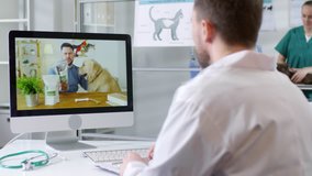 Medium shot of male vet in white coat sitting at his desk and talking on video call with male dog owner asking advice about nutrition and diet