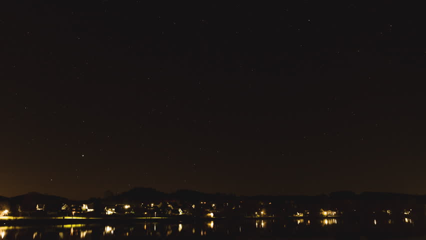 Nightlapse view across waterfront city as stars move across the sky with random light streaks from passing aircraft across the night sky.