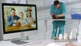 Handheld tracking shot of female vet in scrubs sitting at her desk and writing notes while having video call with family with sick guinea pig