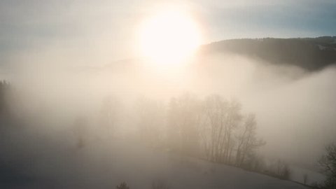 Ascending aerial shot, flying through layers of fog in Snowy landscape near Oberstaufen.