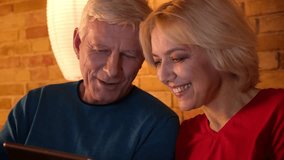 Closeup shoot of aged happy couple watching a comedy on the tablet laughing cheerfully sitting on the sofa indoors in a cozy apartment - Powered by Shutterstock - Get 15% off with code: PIKWIZARD15