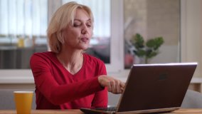 Closeup shoot of aged caucasian woman having a video call on the laptop smiling and talking happily indoors in a cozy apartment