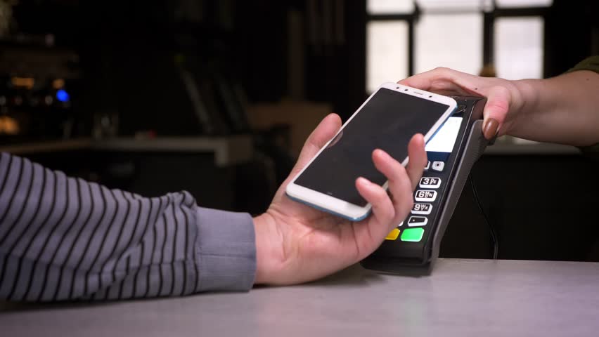 Close-up shot of man applies smartphone to terminal doing contactless payment getting a cup of coffee on gym background. | Shutterstock HD Video #1028450177