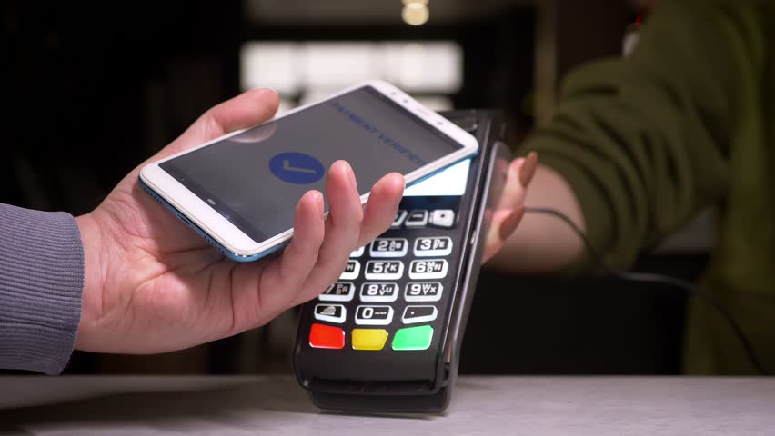 Close-up shot of man applies smartphone to terminal performing successful contactless payment. | Shutterstock HD Video #1028450231