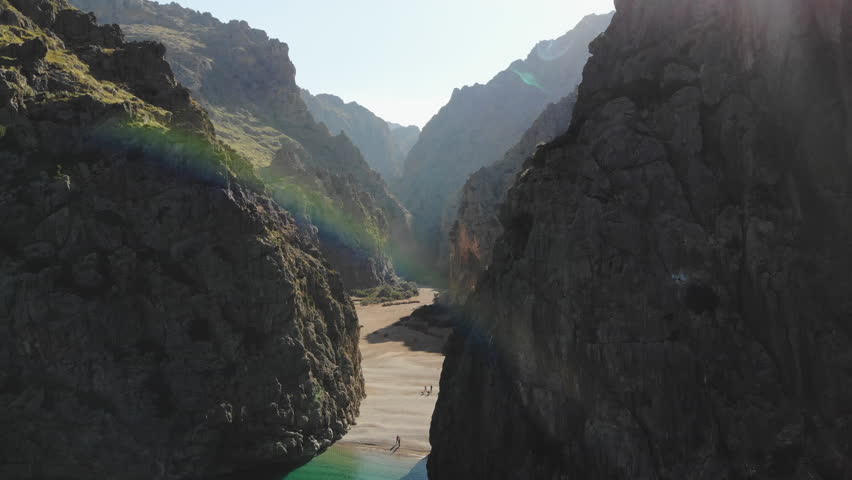 an upward flying drone shot from the from of the iconic rock gap and gorge in the distance and sun flare at the torrent de pareis near Port de Sa Calobra in Majorca