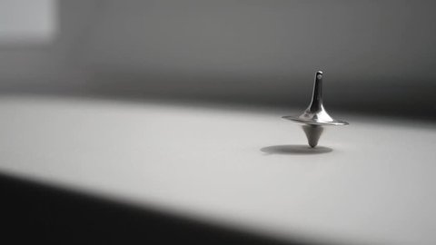 Totem spinning top spinning, wobbling and stopping. Spinning top on white surface. Wobbly Spinning Metal Top Looping Endlessly. Inception theme. 