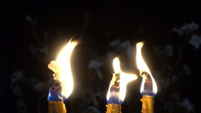 Closeup of three yellow candle burn against darkness on black night in the wind as light for life. Dying out the flame. Candle light for spirituality ceremony or worship. 4K video footage.