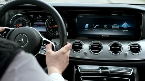 Berlin, Germany - April 16, 2019: Man testing additional car control at Mersedes E 213 car dashboard using modern sensor button on te wheel