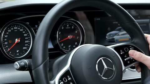 Berlin, Germany - April 16, 2019: Man testing additional car control at Mersedes E 213 car dashboard using modern sensor button on te wheel