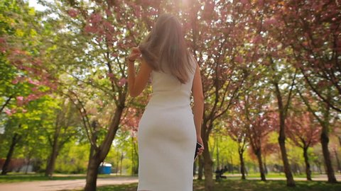 Back view of woman looking at blossom trees in summer park touching hair