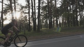 Cycling girl on bicycle. Cycling training. Young beautiful girl cyclist rides bike in the part. Follow shot with sun through trees on the background. Cycling concept. Slow motion