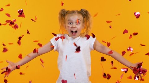Excited girl throwing heart-shaped confetti into air, children party, slow-mo