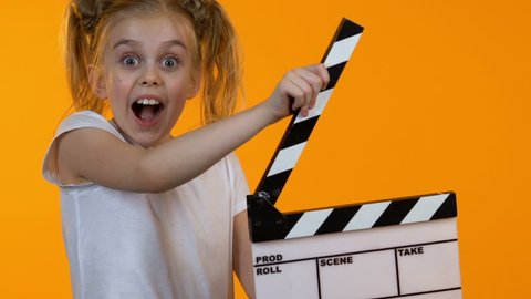Funny little kid using clapboard and smiling on camera, junior acting school