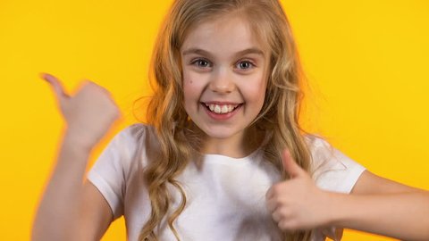 Excited girl showing thumbs-up and winking, successful happy kid on background