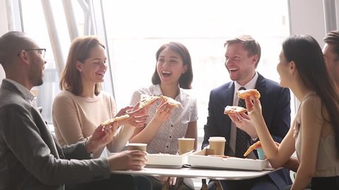 Happy multicultural business team people talking laughing eating pizza together in office, cheerful workers staff group chatting sharing lunch food dinner meal enjoying having fun at work break