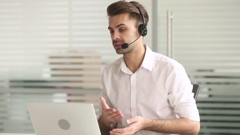Male customer service support agent telemarketer wearing headset looking at laptop make business conference internet video call, businessman consult client in online chat in office by teleconference