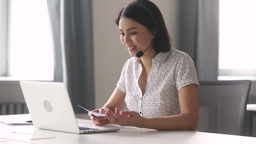 Smiling asian businesswoman call center customer service support agent wear headset talking looking at laptop holding papers, female manager on conference video call consulting client online Royalty-Free Stock Footage #1028495447