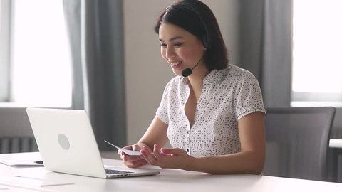 Smiling asian businesswoman call center customer service support agent wear headset talking looking at laptop holding papers, female manager on conference video call consulting client online