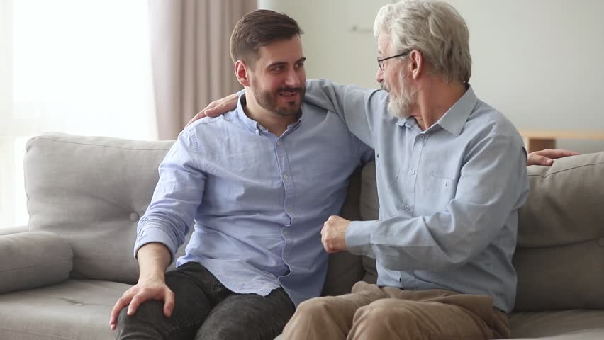 Happy generations old father laughing embracing young son giving fist bump sit on sofa at home, friendly senior dad hug adult man talking joking having fun enjoy time together and good relationships Royalty-Free Stock Footage #1028497853