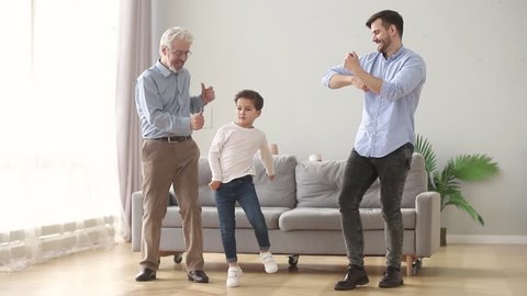 Happy active funny family old grandfather, young dad and cute little child son laughing dancing in modern living room, cheerful grandparent father with kid boy enjoying playing having fun at home toge