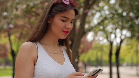 Woman reading message in smartphone walking at summer park