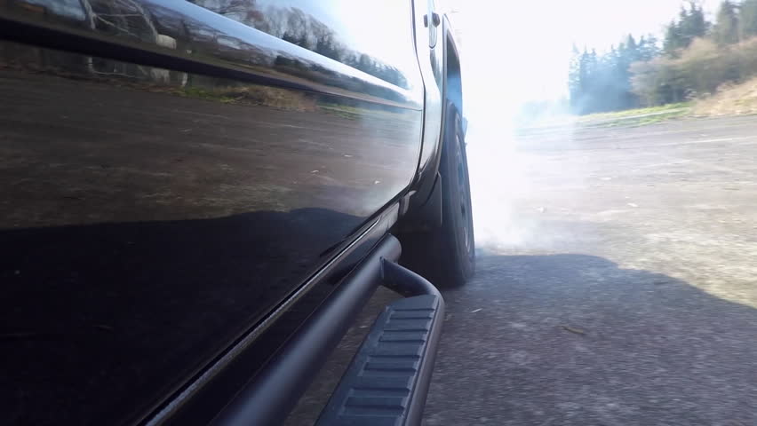 Shot of the rear tire of a black truck doing a burnout on an abandoned parking lot.
