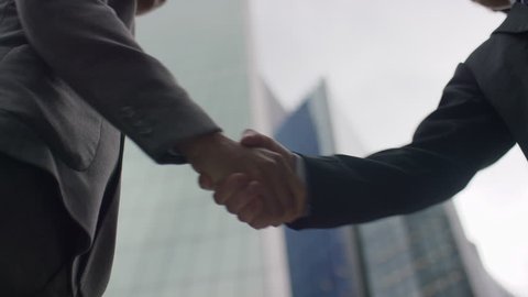Two Asian business men's hands come together for a handshake in the city, in slow motion