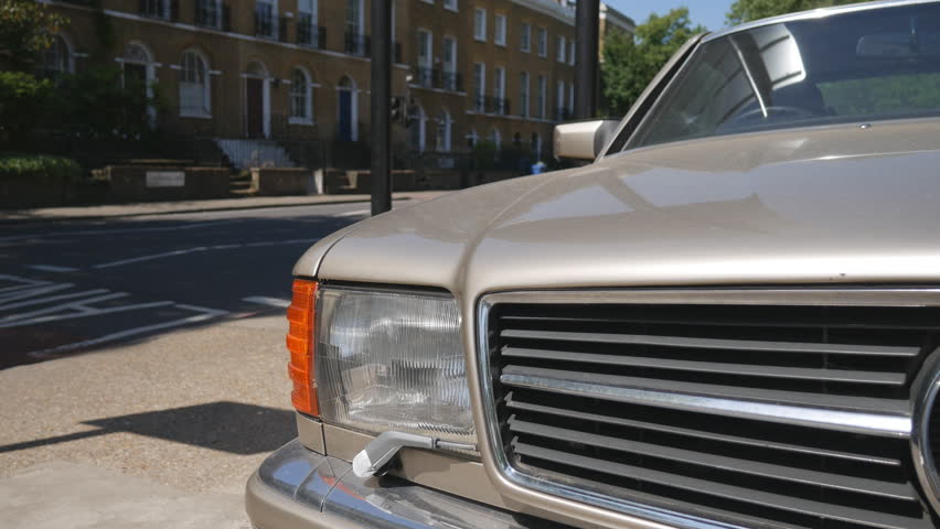 The headlights of an old car on the road standing opposite of a row of houses.